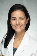 Dr. Hasbún, a smiling woman with dark hair wearing a white coat.