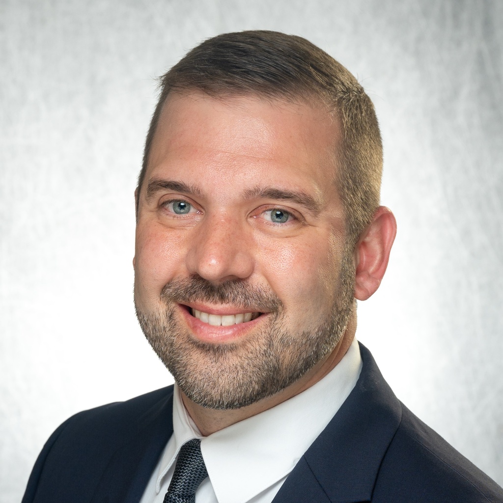 Adam Santi, a bearded man wearing a dark suit jacket.