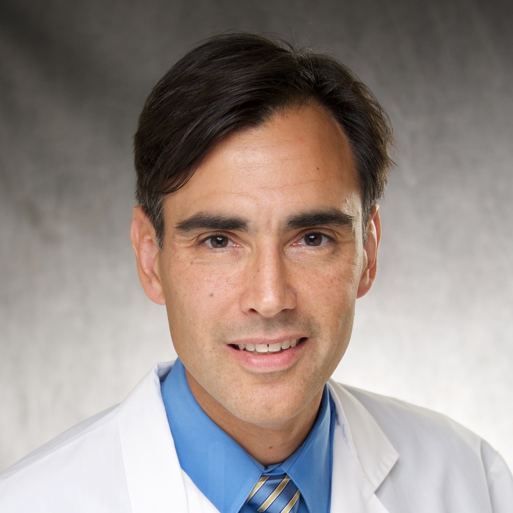 Dr. Swick, a dark-haired man wearing a blue shirt and white coat.