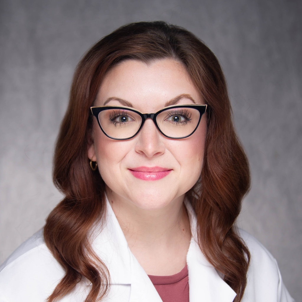 Lauren Paul, a woman wearing black horn-rimmed glasses and a white coat.