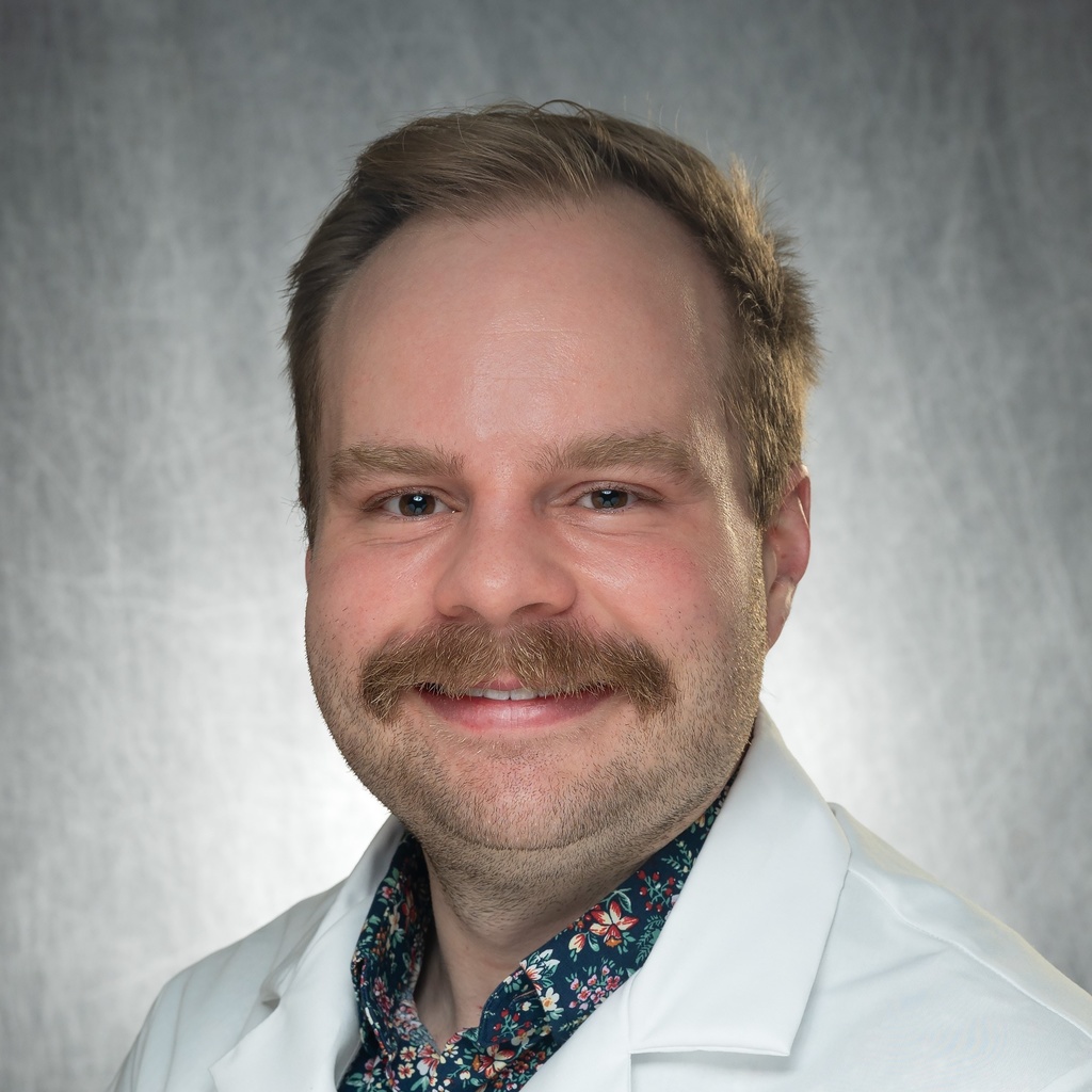 Dr. Palmer, a man with a mustache wearing a floral shirt and white coat.