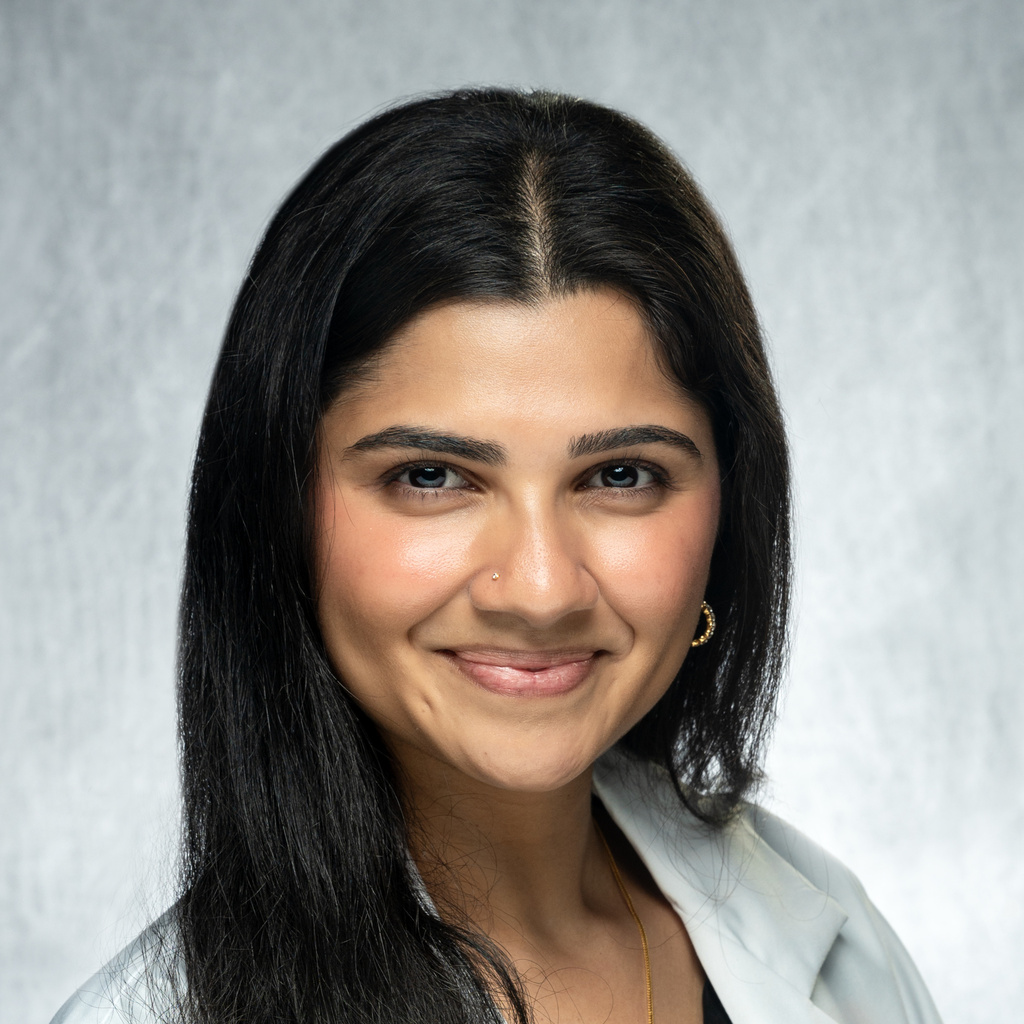 Dr. Mani, a dark-haired woman wearing a black shirt and white coat
