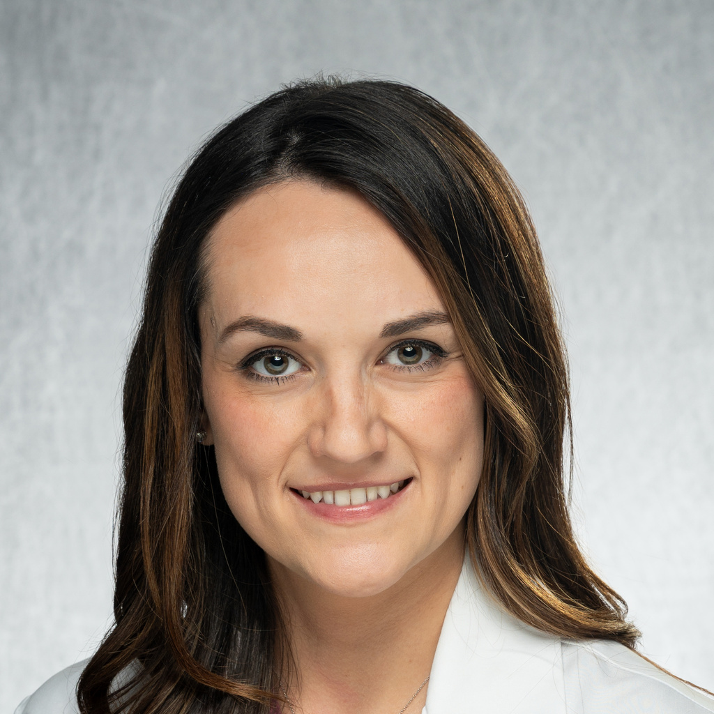 A woman with brown hair wearing a white coat.