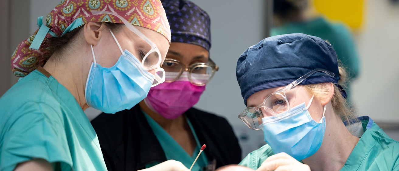 Three doctors wearing face masks examine a patient.